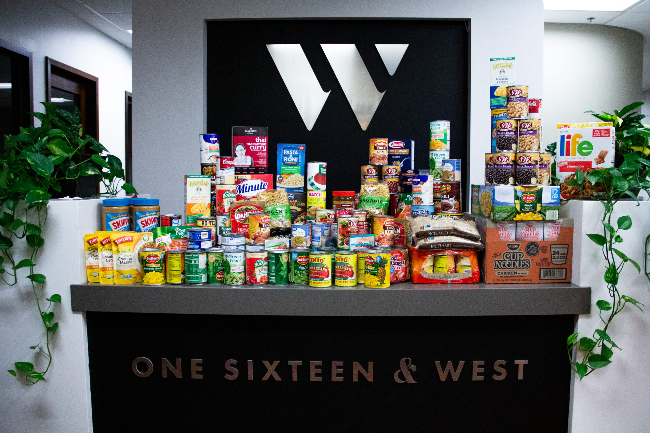 Photo of 116 & West's canned food drive. The front desk of the agency is stacked with various canned an boxed foods.