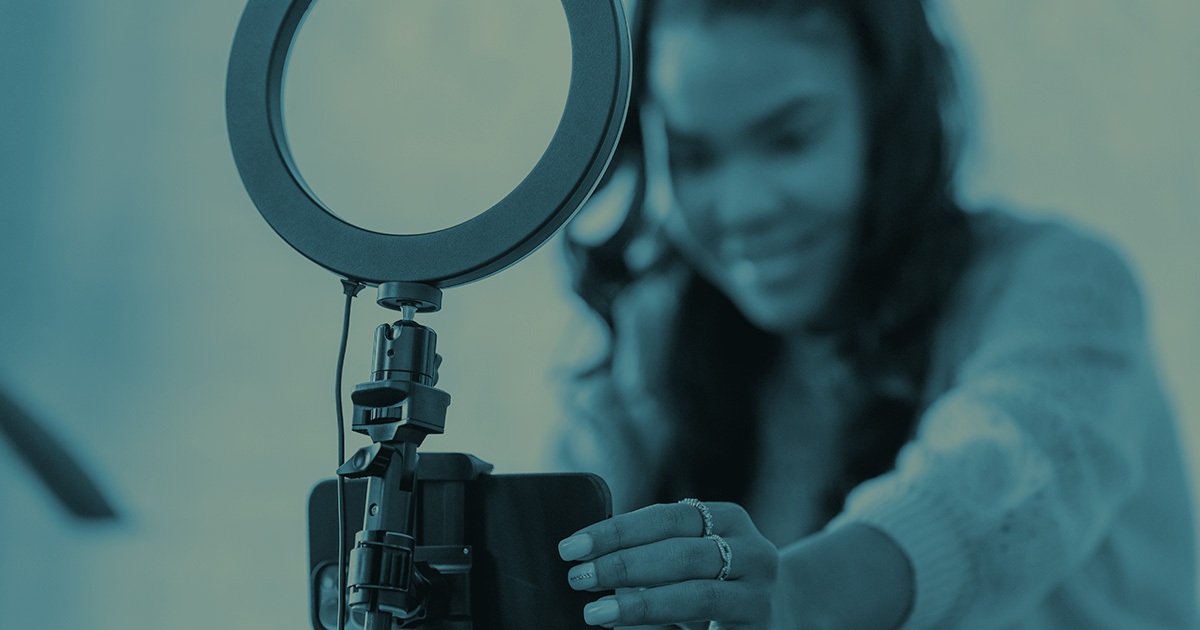 Rectangular image of a woman setting up a camera and ring light.