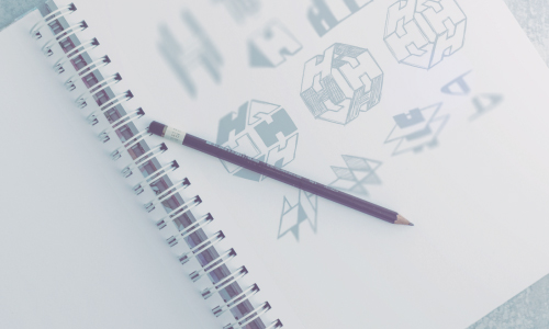 A pencil lying on the pages of an open notebook with drawings of logo thumbnails